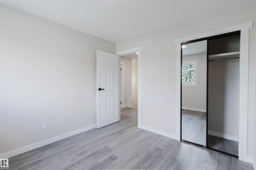 Light-toned wood-finish flooring, white paneled interior door, and mirrored closet doors - 10423 35 Avenue Nw, Edmonton, AB 
