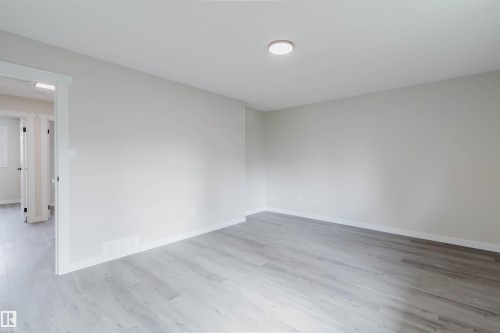 Light wood-finish flooring with white baseboards, a flush-mount ceiling light, and light-toned walls - 10423 35 Avenue Nw, Edmonton, AB 