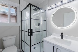 Modern bathroom featuring a black-framed glass shower enclosure, white vanity with integrated sink, illuminated circular mirror, and matte black fixtures - 
