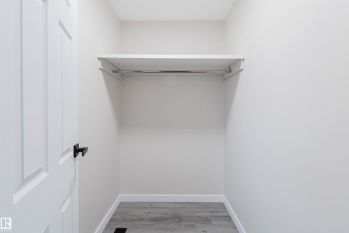 Closet with a single-panel door, black hardware, wood-finish flooring, white walls, and an integrated shelf with a hanging rod - 10423 35 Avenue Nw, Edmonton, AB 