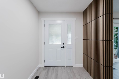 Entryway featuring a white door with frosted glass, an adjacent sidelight, contemporary wood-slat wall paneling, and light wood-finish flooring - 10423 35 Avenue Nw, Edmonton, AB 