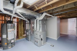 Exposed wood ceiling joists, two furnaces, water heater, painted concrete flooring, and a framed doorway - 