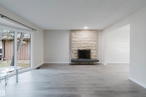 Stone fireplace with a dark floating hearth, wide plank wood-finish flooring, and recessed lighting - 10423 35 Avenue Nw, Edmonton, AB 