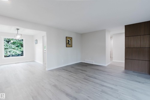 Spacious room with light wood-finish flooring, a contemporary accent wall, and a large window - 10423 35 Avenue Nw, Edmonton, AB 
