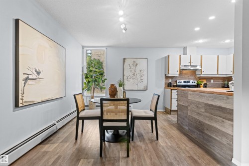 Open-concept living space featuring wood-finish flooring, recessed lighting, a kitchen with white cabinetry, a wood-finish countertop, and a tiled backsplash - #7 10032 113 St Nw, Edmonton, AB 