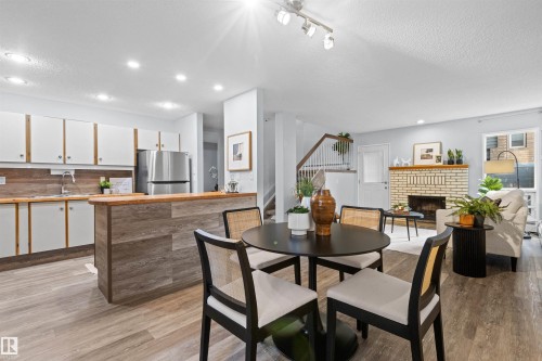 Open-concept living area featuring wood-finish flooring, a kitchen with stainless steel appliances, a brick fireplace, and track lighting - #7 10032 113 St Nw, Edmonton, AB 