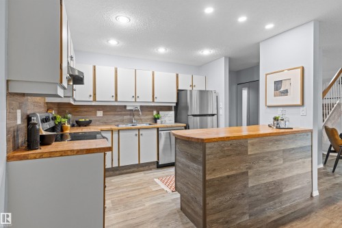 Kitchen featuring white cabinetry with wood-finish trim, wood-finish countertops, stainless steel appliances, and recessed lighting - #7 10032 113 St Nw, Edmonton, AB 