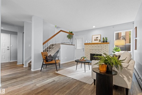 Wood-finish flooring throughout, featuring a white brick fireplace with a wood mantle, a staircase with white spindles and wood handrail, and white panel doors - #7 10032 113 St Nw, Edmonton, AB 