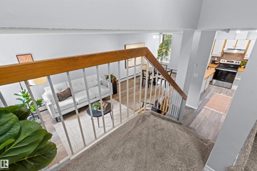 Carpeted staircase with wood railing, leading to an open-concept living area with wood-finish flooring, a dining space, and a kitchen featuring white cabinetry, light countertops, and stainless steel appliances - #7 10032 113 St Nw, Edmonton, AB 