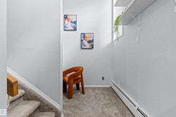 Carpeted stairs with wood handrail, light gray wall finishes, and wall-mounted shelving - 