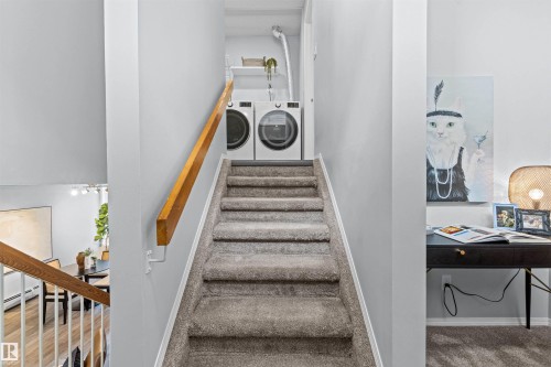 Carpeted staircase with wood-finish handrail leading to a stacked laundry appliance area - #7 10032 113 St Nw, Edmonton, AB 