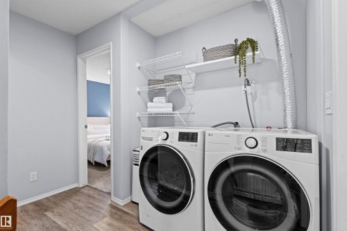 Laundry area featuring front-load appliances, wire shelving, and wood-finish flooring - #7 10032 113 St Nw, Edmonton, AB 