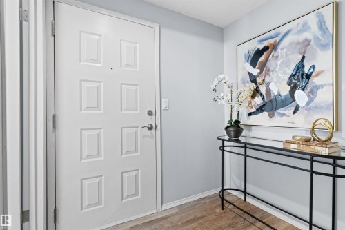 Entryway featuring a paneled door with hardware, neutral wall paint, and wood-finish flooring - #7 10032 113 St Nw, Edmonton, AB 