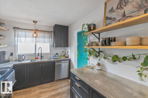 Kitchen featuring wood-finish flooring, dark cabinetry, a stainless steel dishwasher, and open shelving - 8808 43 Avenue Nw, Edmonton, AB 