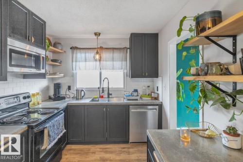 Kitchen featuring dark cabinetry, stainless steel appliances, subway tile backsplash, wood-finish flooring, and open shelving - 8808 43 Avenue Nw, Edmonton, AB 