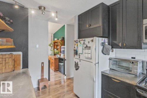 Kitchen featuring dark cabinetry, a white tile backsplash, track lighting, and concrete-finish countertops - 8808 43 Avenue Nw, Edmonton, AB 