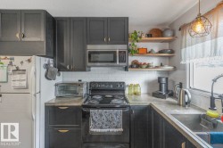 Kitchen featuring black cabinetry, white subway tile backsplash, stainless steel microwave, and open wood-finish shelving - 