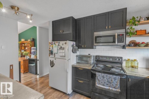 Black cabinetry with gold-tone hardware, stainless steel microwave, white subway tile backsplash, light-toned countertops, and wood-finish flooring - 8808 43 Avenue Nw, Edmonton, AB 