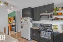 Black cabinetry with gold-tone hardware, stainless steel microwave, white subway tile backsplash, light-toned countertops, and wood-finish flooring - 