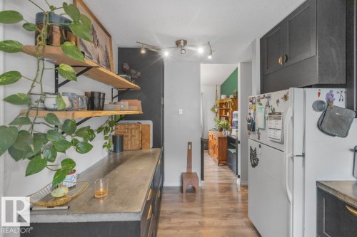 Dark cabinetry with gold-toned hardware, wood-finish flooring, recessed lighting, and open wood shelving - 8808 43 Avenue Nw, Edmonton, AB 