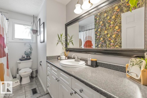 Bathroom with an expansive vanity featuring an integrated sink, white cabinetry with dark hardware, a framed mirror, and a window - 8808 43 Avenue Nw, Edmonton, AB 