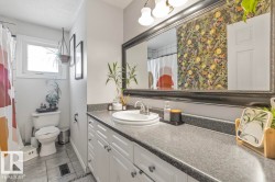 Bathroom with an expansive vanity featuring an integrated sink, white cabinetry with dark hardware, a framed mirror, and a window - 