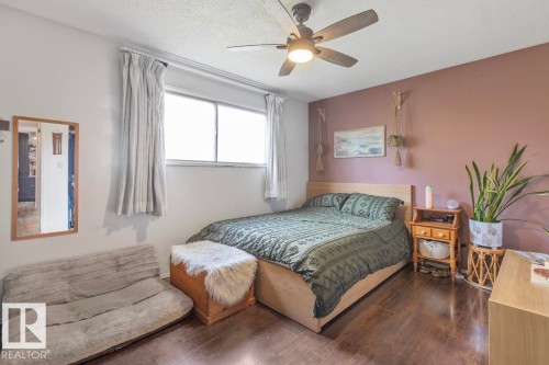 Hardwood-style flooring, light wood bed frame, ceiling fan with integrated lighting, and window with curtain treatments - 8808 43 Avenue Nw, Edmonton, AB 