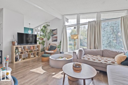 Sloped ceiling with exposed beams, wood-finish flooring, multiple large windows, and a built-in shelving unit - 8808 43 Avenue Nw, Edmonton, AB 