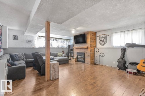 Spacious room featuring wood-finish flooring, a built-in fireplace with a wood-paneled surround, a wood mantel, and multiple windows - 8808 43 Avenue Nw, Edmonton, AB 