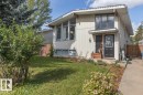 Split-level residence featuring a dark paneled entry door, vertical siding, and an established front lawn - 8808 43 Avenue Nw, Edmonton, AB 