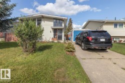 Split-level residence featuring a concrete driveway, established front landscaping, an exterior storage shed, and a fenced side yard - 