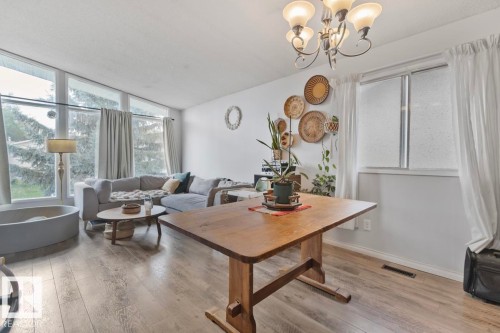 Spacious living area featuring wood-finish flooring, a multi-pane picture window, a secondary window, and an overhead chandelier - 8808 43 Avenue Nw, Edmonton, AB 