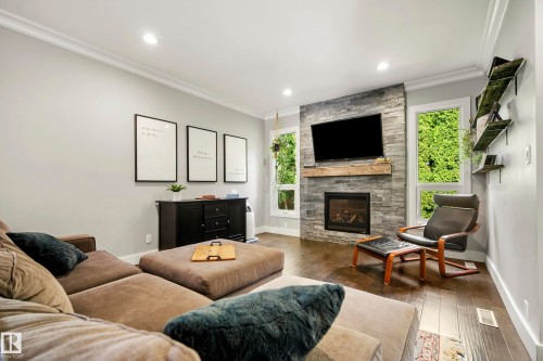 Stone-clad fireplace with wood mantel, recessed lighting, crown molding, wood-finish flooring, and built-in shelving - 11 Brunswick Crescent, St. Albert, AB 