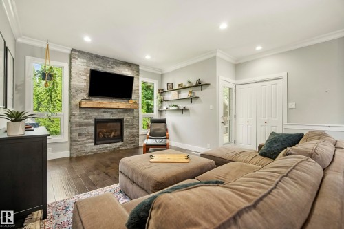 Living area featuring a stone-clad fireplace with wood mantel, recessed lighting, wood-finish flooring, and multiple windows - 11 Brunswick Crescent, St. Albert, AB 