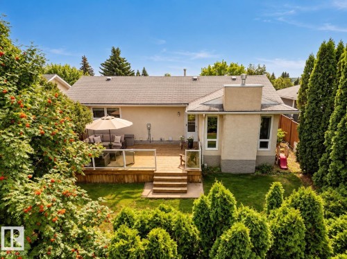 Expansive backyard featuring a wood deck with glass railing, manicured lawn, mature trees, and a stucco exterior - 11 Brunswick Crescent, St. Albert, AB 