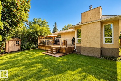Spacious green lawn, wood deck with glass railing, stucco exterior, multiple windows, and a storage shed - 11 Brunswick Crescent, St. Albert, AB 