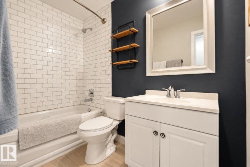 Bathroom featuring white subway tile surround, a white vanity with an integrated sink, a framed mirror, and wood-finish flooring - 11 Brunswick Crescent, St. Albert, AB 