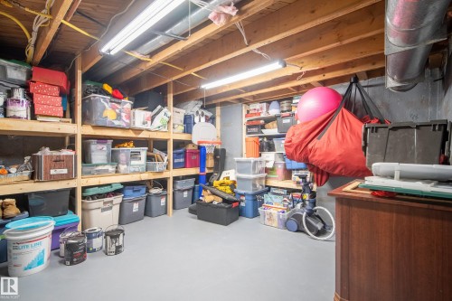Unfinished basement with exposed wood joists, concrete walls, painted concrete flooring, extensive built-in wood shelving, and fluorescent lighting - 11 Brunswick Crescent, St. Albert, AB 