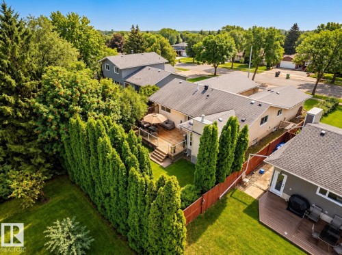 Expansive backyard with a wood deck, glass panel railings, and mature privacy trees - 11 Brunswick Crescent, St. Albert, AB 