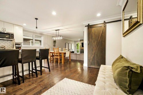 Wood-finish flooring throughout, kitchen with white cabinetry and subway tile backsplash, dining area with a linear chandelier, and a wood barn door - 11 Brunswick Crescent, St. Albert, AB 