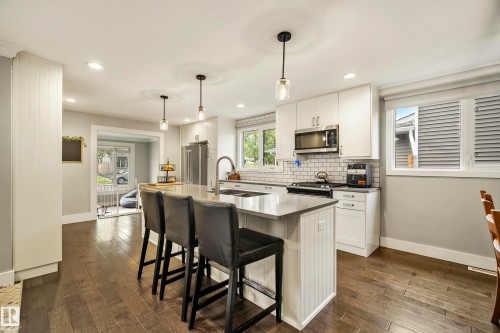 Kitchen featuring an island with seating, stainless steel appliances, subway tile backsplash, white cabinetry, and wood-finish flooring - 11 Brunswick Crescent, St. Albert, AB 