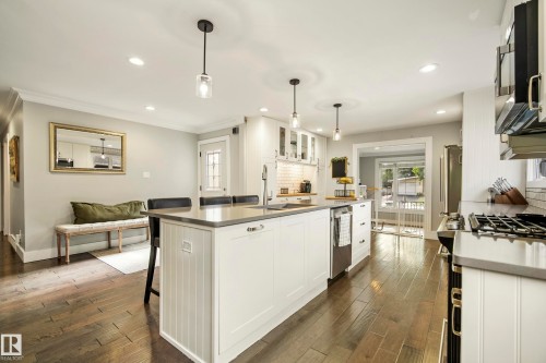 Kitchen featuring wood-finish flooring, recessed lighting, a central island with countertop seating, stainless steel appliances, and white cabinetry with subway tile backsplash - 11 Brunswick Crescent, St. Albert, AB 