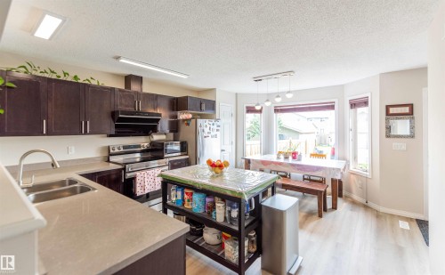 Kitchen featuring dark wood-finish cabinetry, light-toned countertops, stainless steel appliances, and a double basin sink - 8527 Ellis Link Nw, Edmonton, AB - Indoor Photo Showing Kitchen With Double Sink