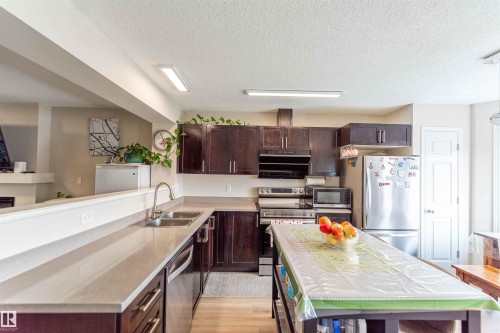Kitchen featuring dark wood-finish cabinetry, light-toned countertops, and stainless-steel appliances - 8527 Ellis Link Nw, Edmonton, AB - Indoor Photo Showing Kitchen With Double Sink