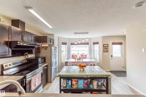 Open-concept kitchen with dark wood cabinetry, stainless steel appliances, light wood-finish flooring, and a bay window dining area - 8527 Ellis Link Nw, Edmonton, AB - Indoor Photo Showing Kitchen