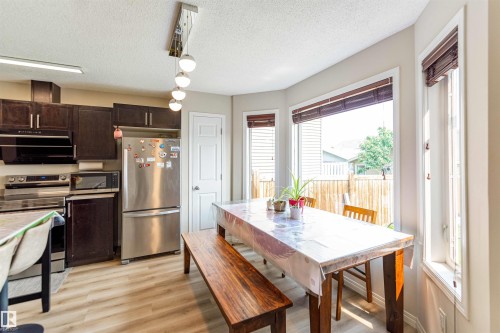 Kitchen and dining area featuring dark wood-finish cabinetry, stainless steel appliances, and wood-finish flooring - 8527 Ellis Link Nw, Edmonton, AB - Indoor Photo Showing Other Room