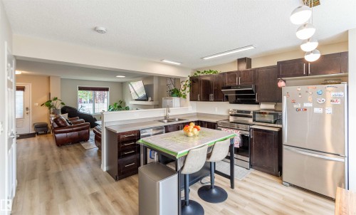Kitchen featuring dark wood cabinetry, stainless steel appliances, a double basin sink, and wood-finish flooring - 8527 Ellis Link Nw, Edmonton, AB - Indoor Photo Showing Kitchen With Double Sink