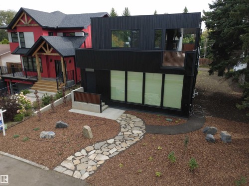 Modern exterior featuring dark vertical siding, a stone pathway, a second-story balcony with wood railings, a concrete entry, and a landscaped front yard with wood chip ground cover - 8815 142 Street Nw, Edmonton, AB 