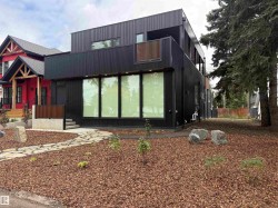 Modern exterior with black vertical siding, multiple large windows, and a second-story balcony with wood-finish railing - 
