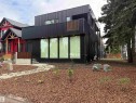Modern exterior with black vertical siding, multiple large windows, and a second-story balcony with wood-finish railing - 8815 142 Street Nw, Edmonton, AB 